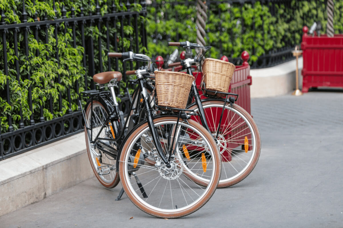 Dve črni mestni kolesi s košarama ob parku. 