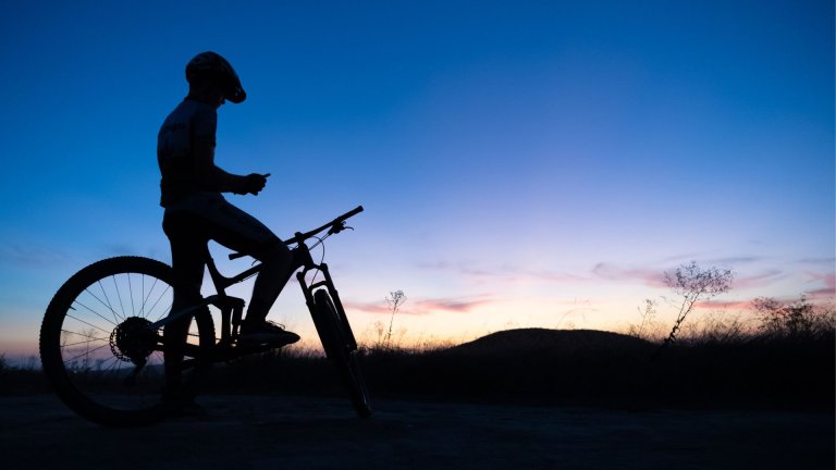 Kolesar ob sončnek zahodu gleda na telefon.